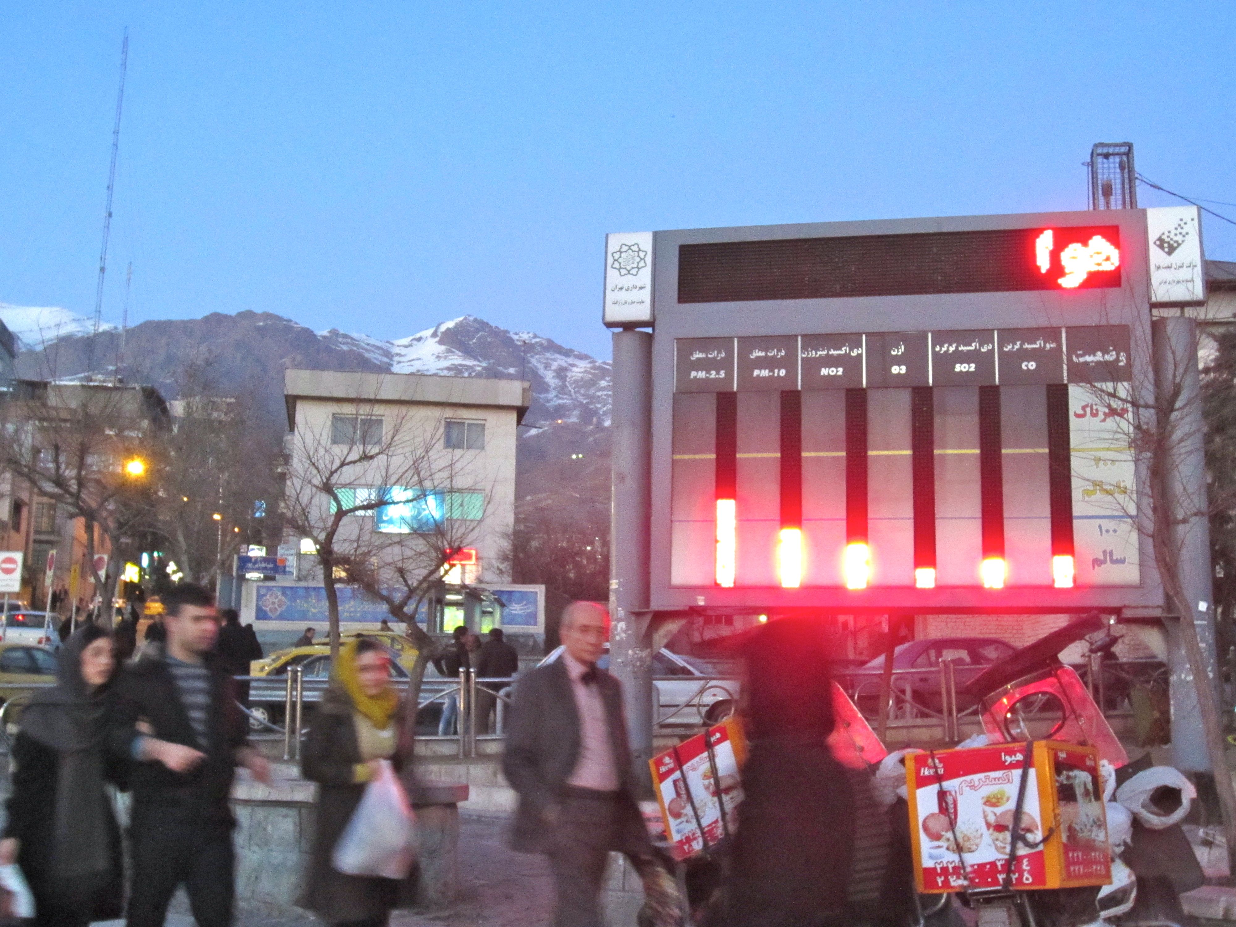 An electronic display monitors air quality in Tajrish Square, north Tehran. The screen displays levels of various toxins in the air alongside reminders to utilize public transportation. The word at the top is the beginning of a reminder, though so far only the war "air" is visible.